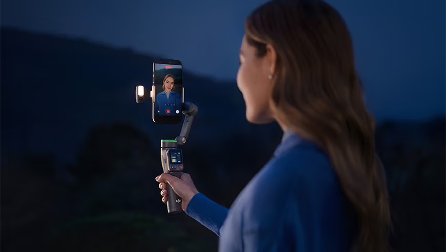 Osoba nagrywa wideo wieczorem po zachodzie słońca korzystając z gimbala DJI Osmo Mobile 8P.