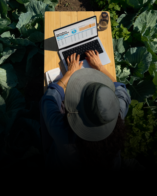 Osoba siedząca przy stole w plenerze i pracująca na srebrnym 14‑calowym MacBooku Pro, niepodłączonym do ładowania