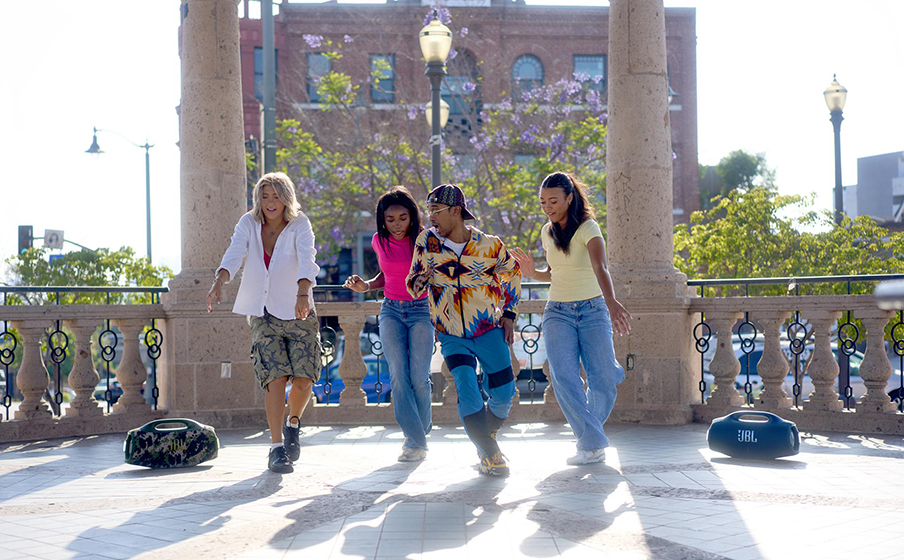 Grupa osób słucha muzyki z kilku głośników JBL Boombox 4 połączonych przez Auracast™