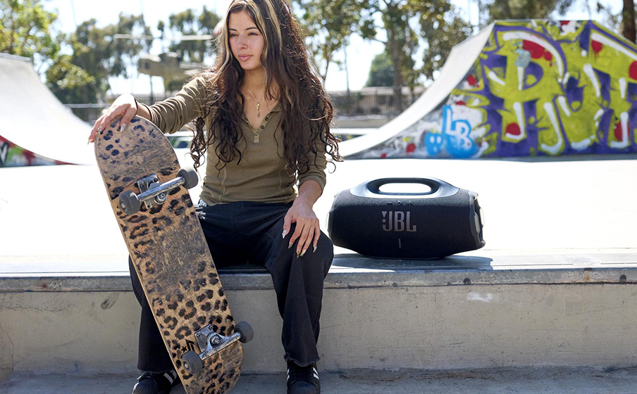 Osoba z deskorolką słucha muzyki z głośnika JBL Boombox 4.