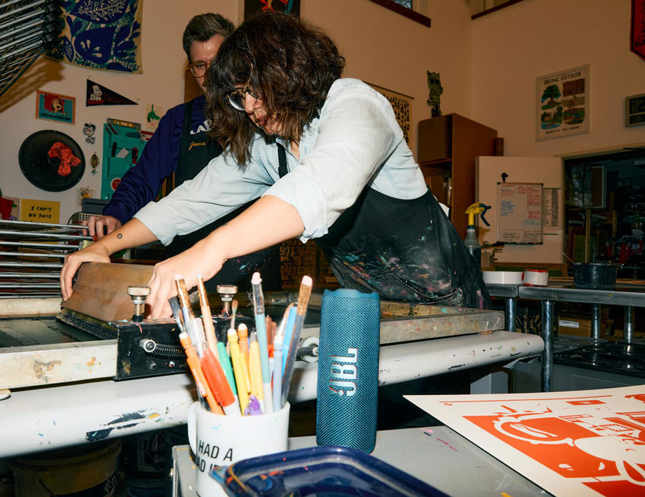 JBL Flip 7 – głośnik odtwarza muzykę w warsztacie drukarskim. Ilustruje długi czas pracy głośnika na akumulatorze.