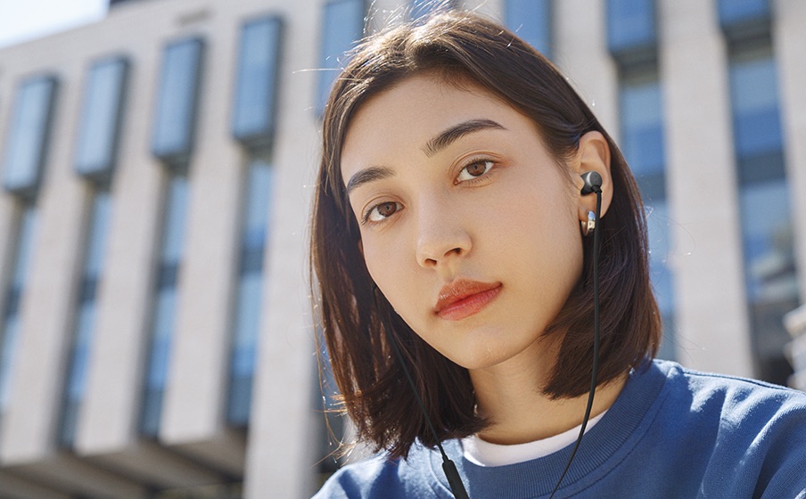 Osoba ze słuchawkami JBL Tune 310C na tle budynku.