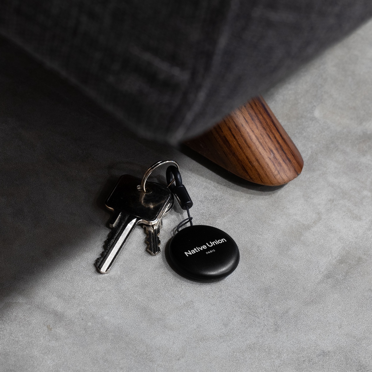 Native Union Find it Tag Lokalizator przypięty do pęku kluczy leży na podłodze pod fotelem.