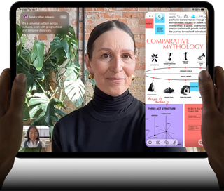 Widoczny od przodu ustawiony poziomo iPad Pro w kolorze gwiezdnej czerni, zaokrąglone rogi, czarna ramka wyświetlacza. Ręce trzymają urządzenie z lewej i prawej strony, na ekranie tłumaczona na żywo rozmowa przez FaceTime. Widać też aplikację edukacyjną z prezentacją „Comparative Mythology”, z tekstem, diagramami i odręcznymi notatkami