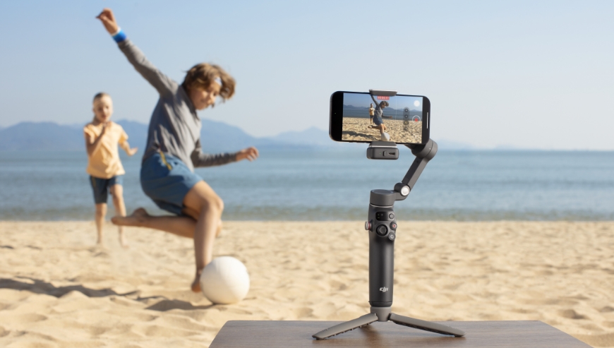 Smartfon na gimbalu DJI Osmo Mobile 7P nagrywa chłopców grających w piłkę na plaży.