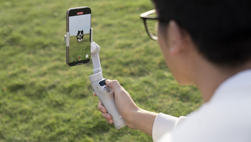 Uzytkownik filmuje biegnącego psa korzystająch z inteligentnego trybu nagrywania obsługiwanego przez gimbal DJI Osmo Mobile 7.