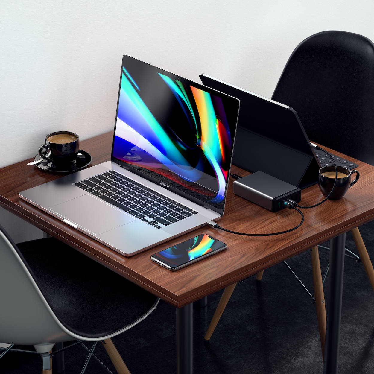 Ładowarka Satechi Desktop 108W Pro 108W 2x USB-C PD 2x USB-A znajduje się na stoliku pomiędzy dwoma laptopami. Ilustracja nowoczesnego designu ładowarki Satechi.