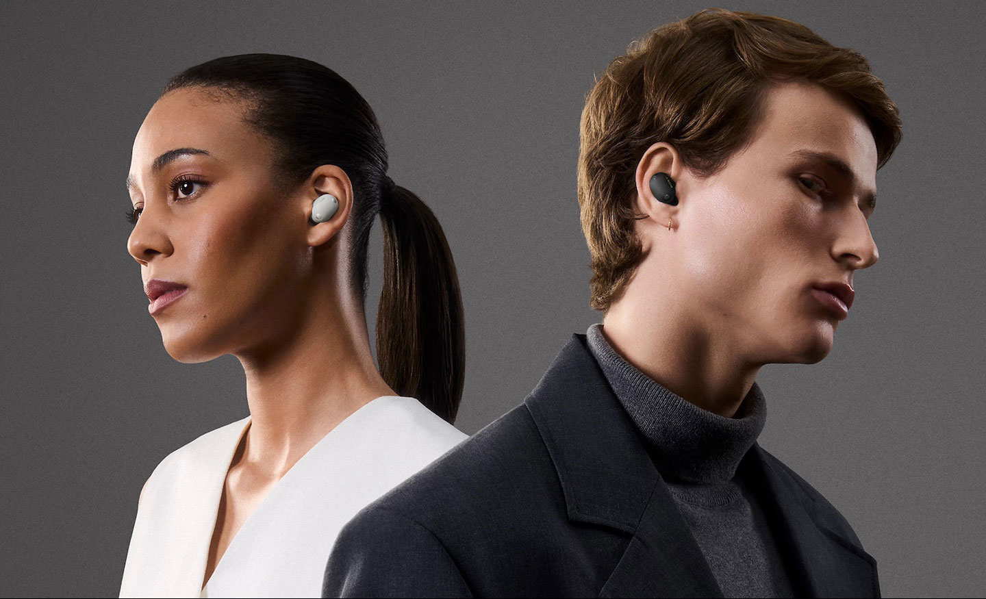 Sony WF-1000XM6 Ujęcie z boku przedstawiające młodą kobietę w bieli z białą słuchawką douszną w uchu. Odwrócony od niej młody mężczyzna w czarno-szarym stroju ma w drugim uchu czarną słuchawkę.