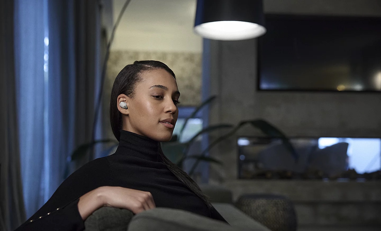 Sony WF-1000XM6 Młoda kobieta ubrana na czarno w zrelaksowanym otoczeniu, z białą słuchawką douszną w uchu.