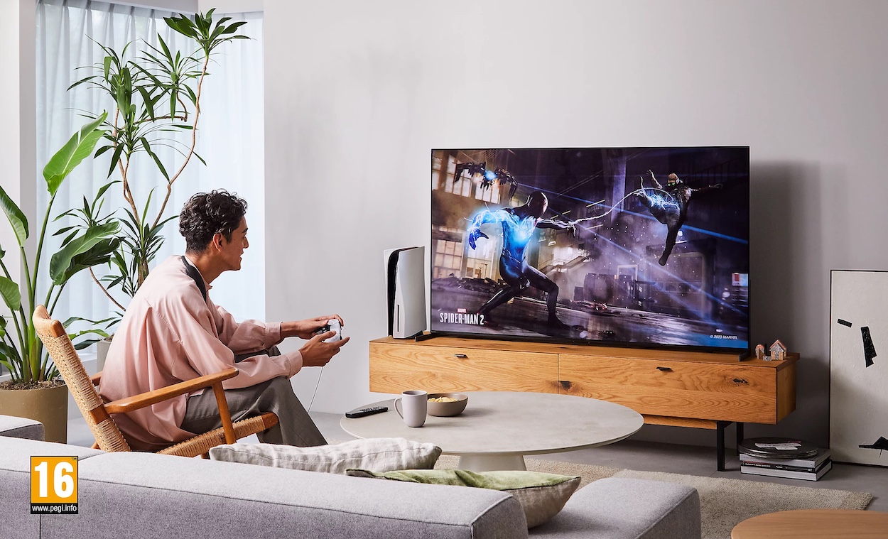 Osoba siedząca w fotelu w domowym salonie, używająca głośnika BRAVIA Theatre U podczas gry na dużym telewizorze