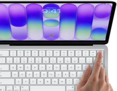 MacBook Neo w kolorze srebrnym z widocznym ekranem logowania i palcem osoby używającej czytnika Touch ID w prawym górnym rogu klawiatury