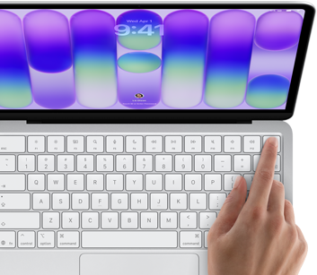 MacBook Neo w kolorze srebrnym z widocznym ekranem logowania i palcem osoby używającej czytnika Touch ID w prawym górnym rogu klawiatury
